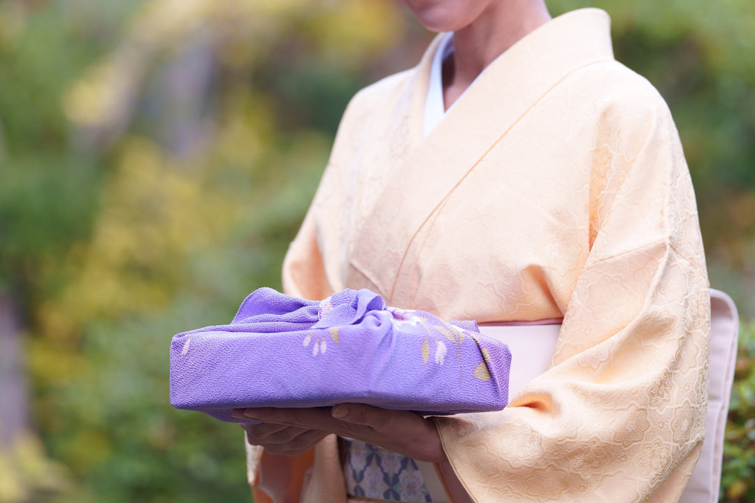 A Japanese woman in a kimono holding a furoshiki wrap in her hands.
