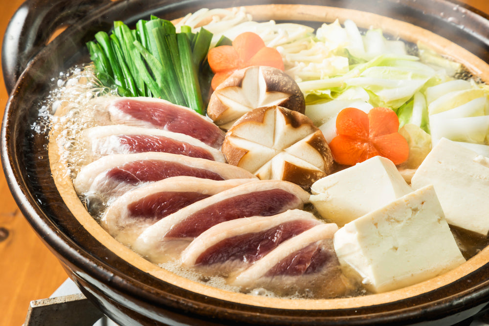 A bubbling pot of nabe hot pot with meat, tofu, mushrooms, and carrots.
